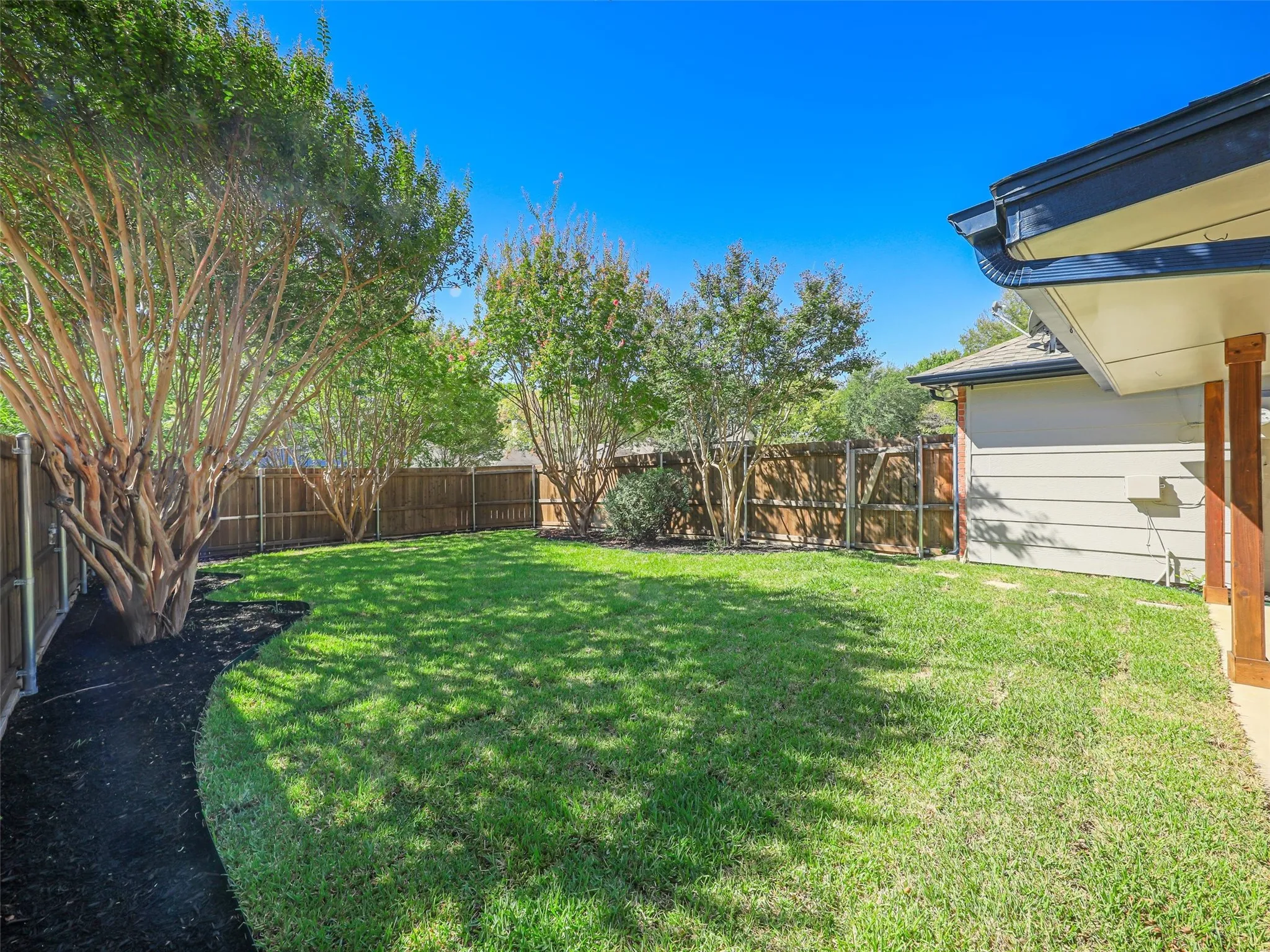 Expansive backyard with a manicured lawn, established trees, and a privacy fence
