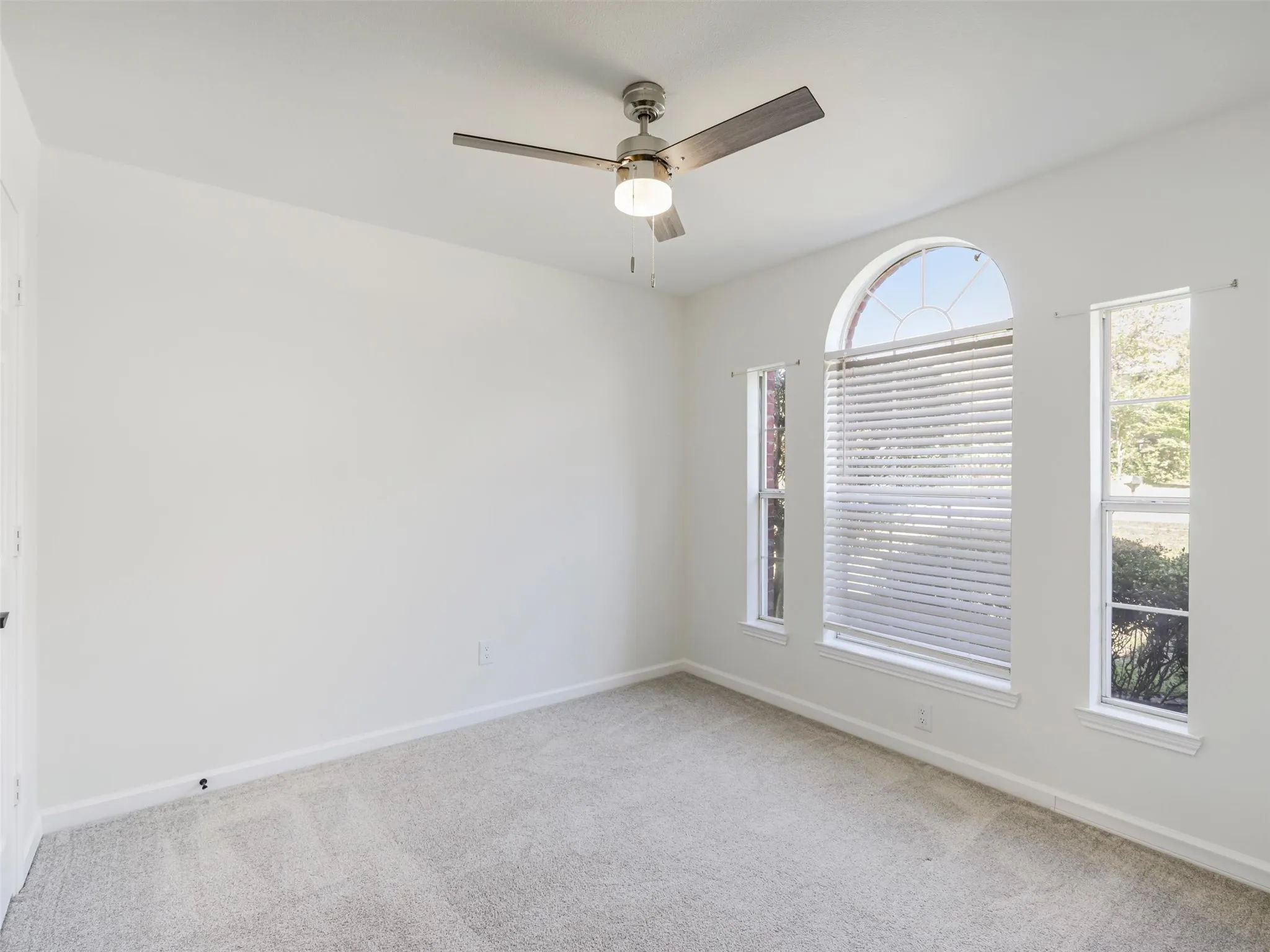 Arched window with two vertical windows, light grey carpeting, and a ceiling fan with integrated lighting