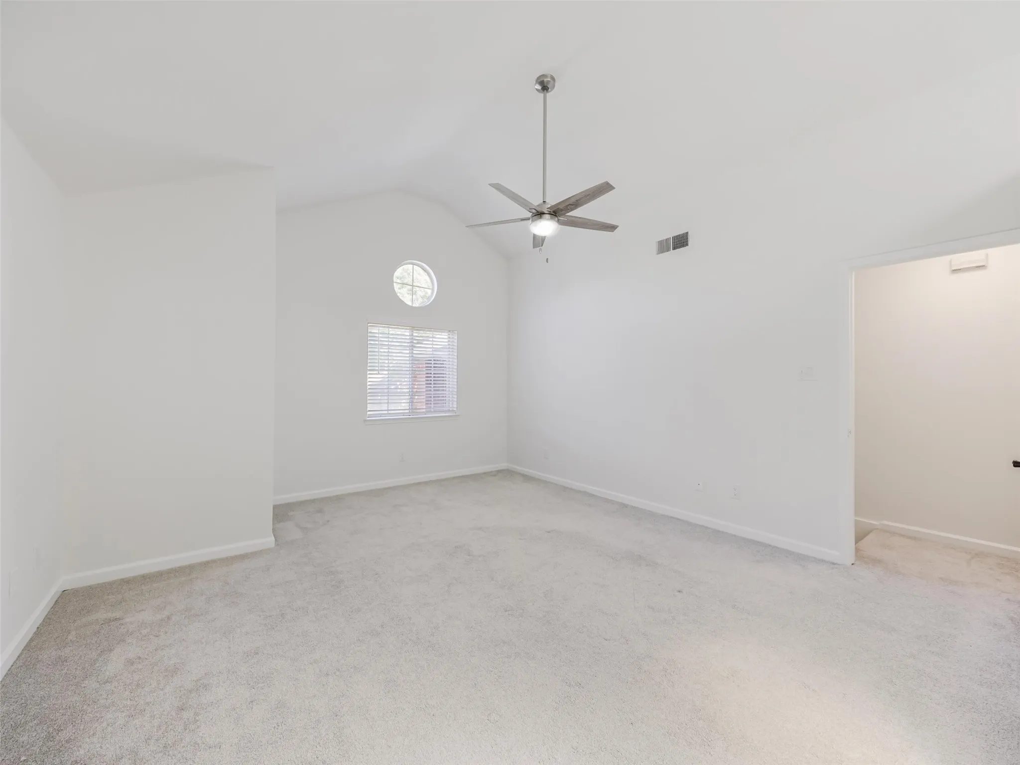 Vaulted ceiling featuring a ceiling fan, light gray carpet, and two windows with blinds
