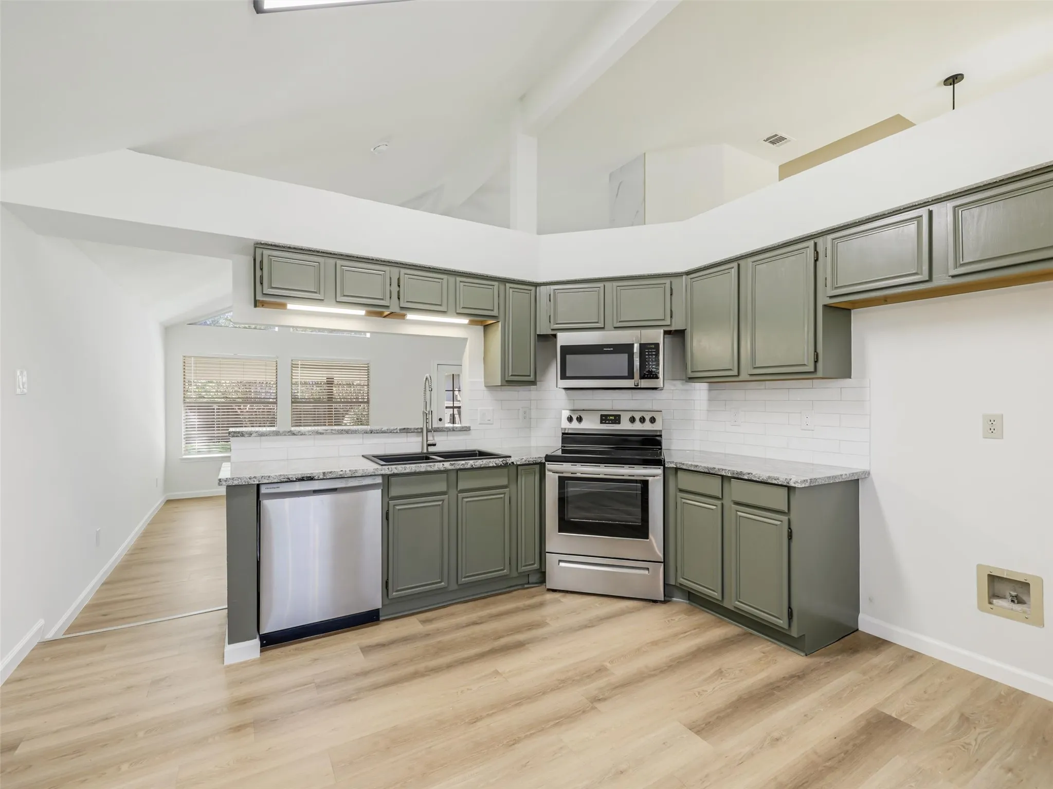Kitchen featuring wood-finish flooring, stainless steel appliances, grey cabinetry, white subway tile backsplash, and light-toned countertops