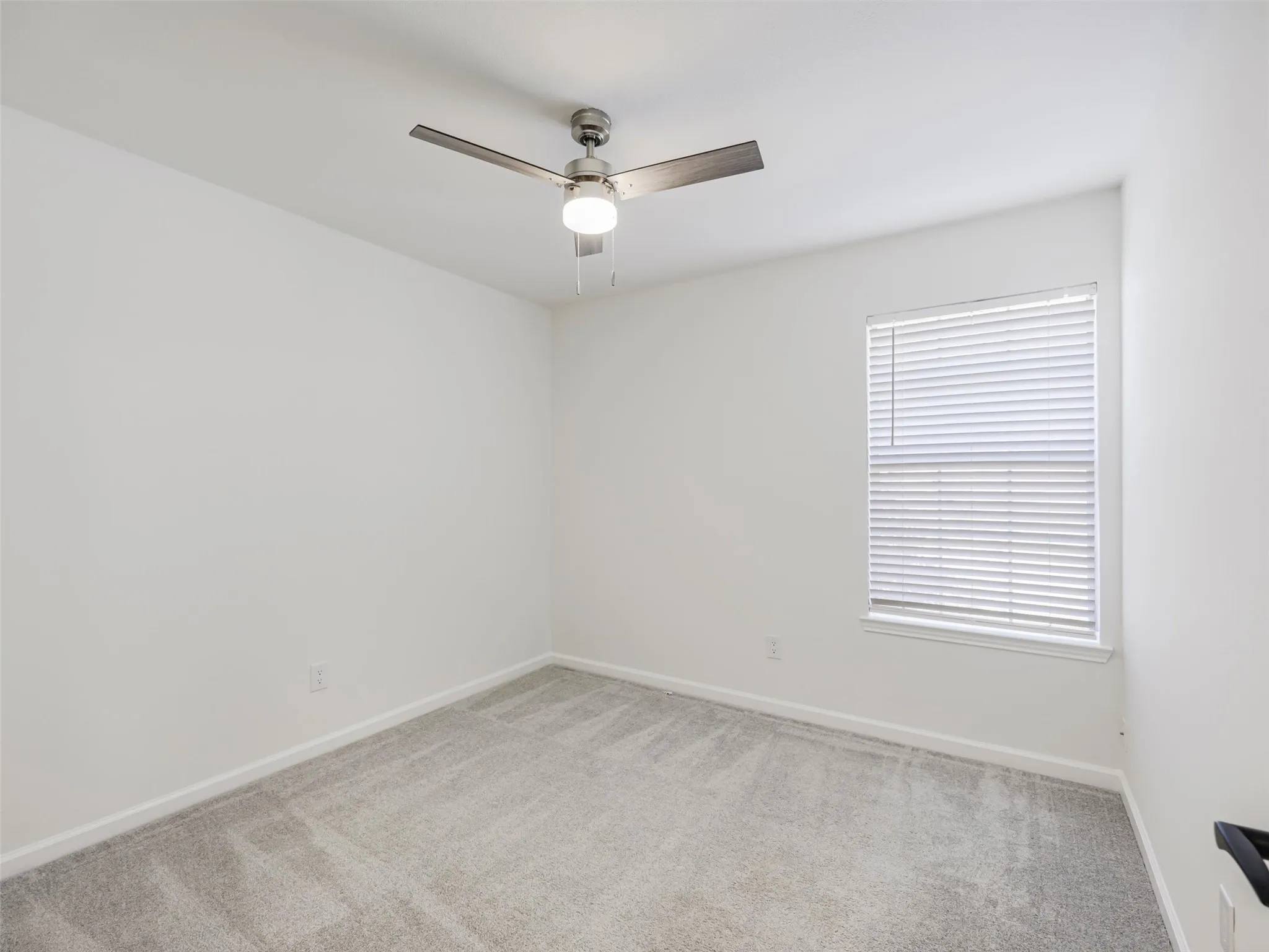 Neutral wall paint, ceiling fan with integrated lighting, window with blinds, and carpeted flooring