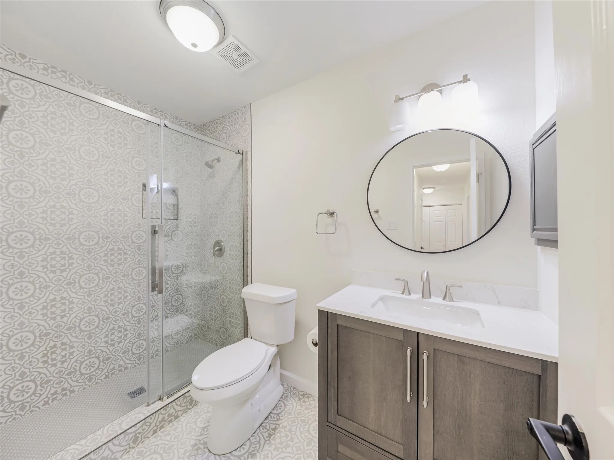 Glass-enclosed shower with patterned tile surround, built-in shower bench, and hexagonal tile flooring