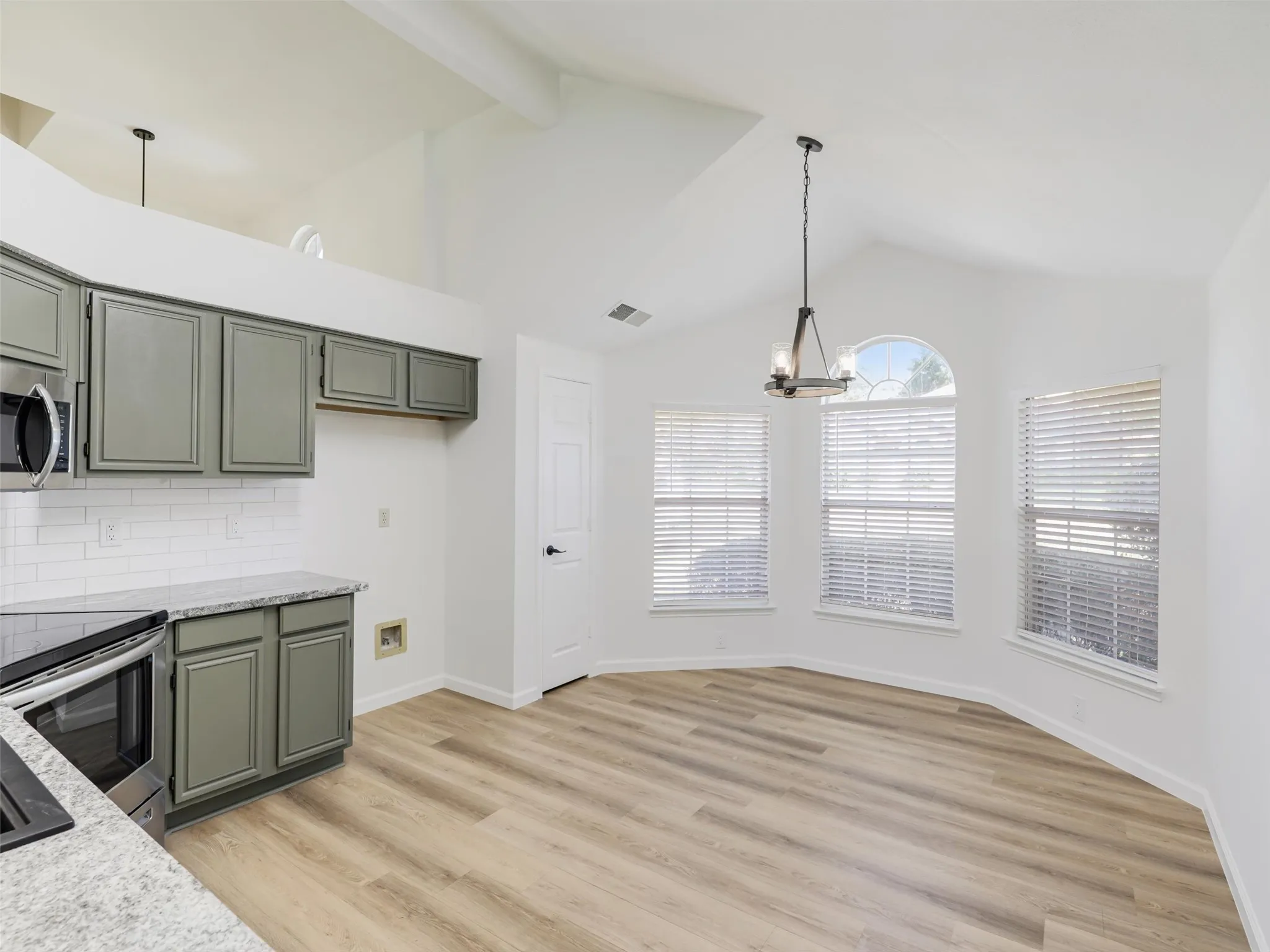 Vaulted ceiling, wood-finish flooring, gray cabinetry, granite-style countertops, and a subway tile backsplash