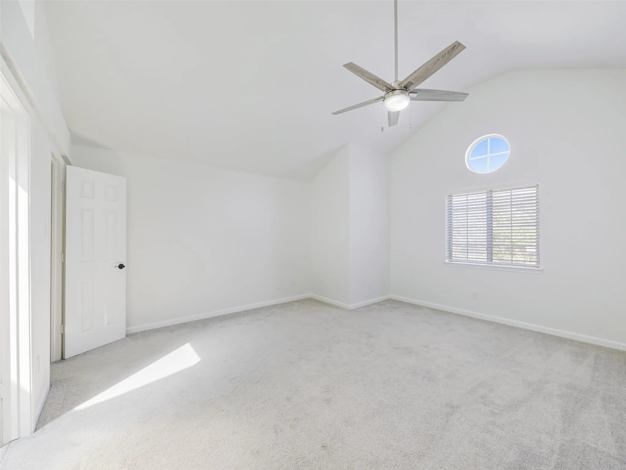 Vaulted ceiling with an integrated ceiling fan, light-toned carpeting, and a round accent window
