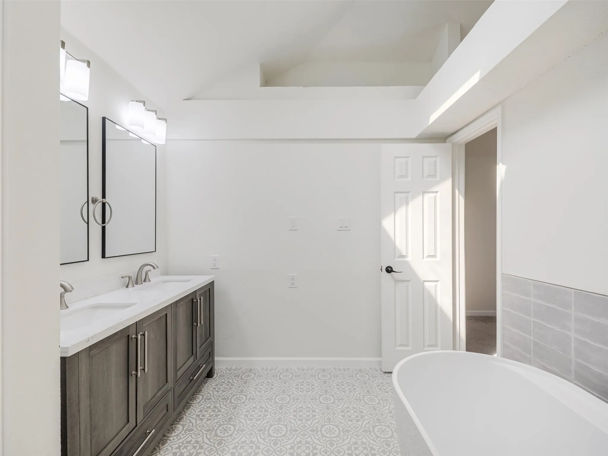 Dual vanity with integrated sinks, patterned tile flooring, freestanding soaking tub, and tile wainscoting