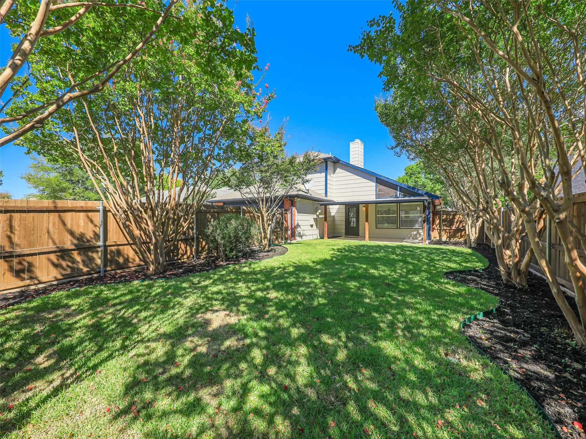 Expansive lawn with mature trees, a covered patio, and wood privacy fencing
