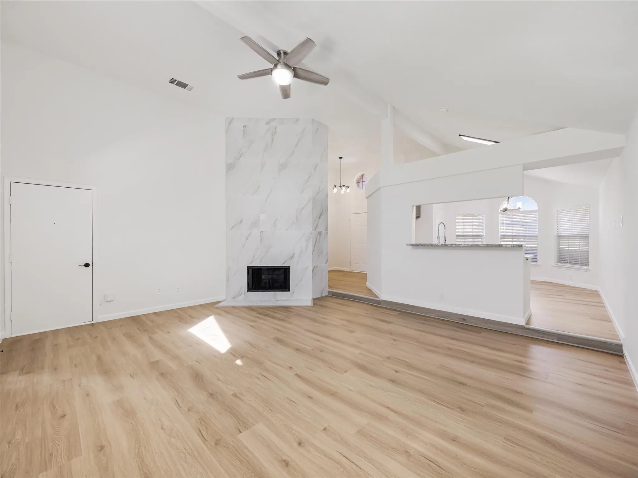 Vaulted ceilings with a ceiling fan, fireplace with a marble-finish surround, wood-finish flooring, and a breakfast bar with a stone-finish countertop