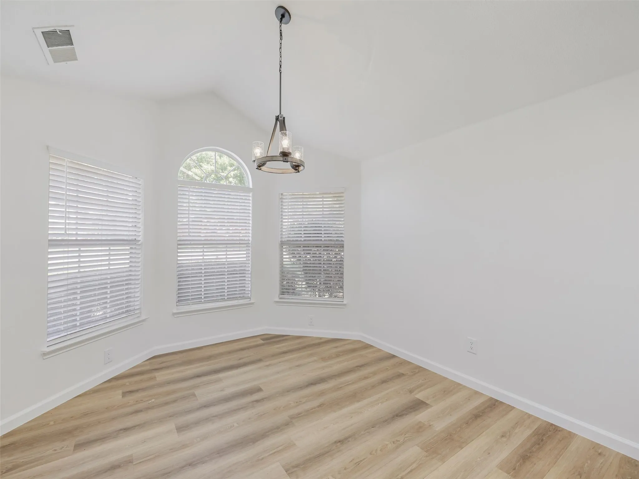 Vaulted ceiling with an industrial-style chandelier, arched window, multiple windows with blinds, and wood-finish flooring