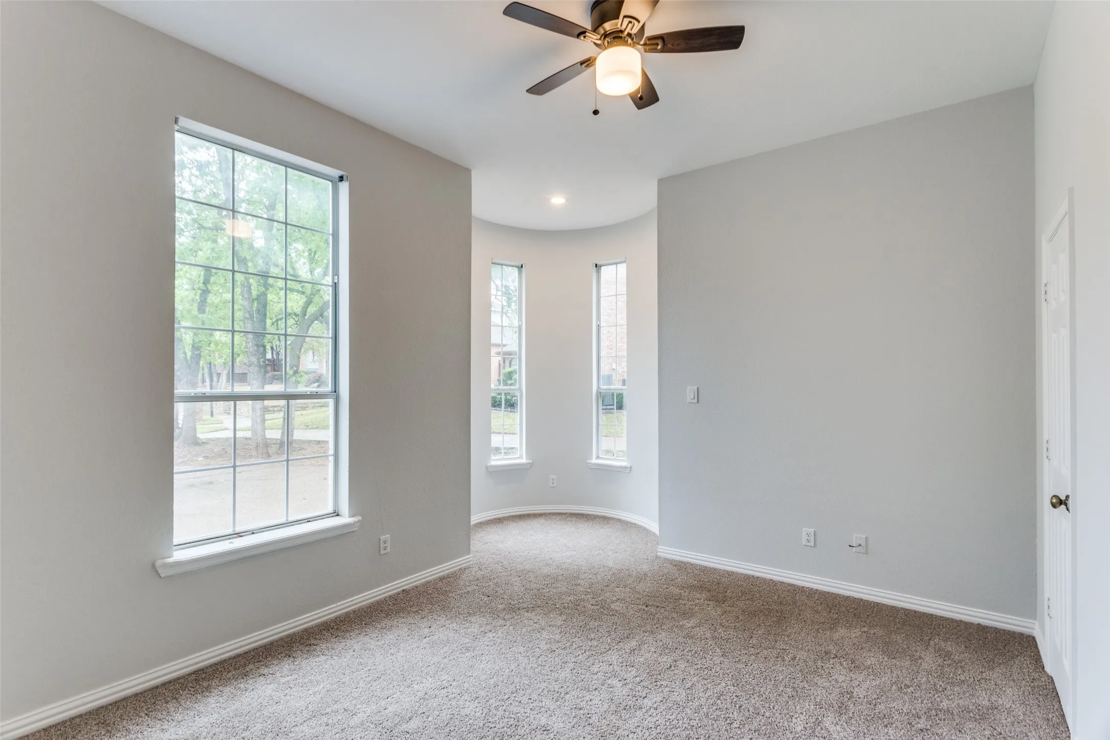 Carpeted room featuring multiple windows, a ceiling fan with integrated lighting, and neutral wall tones