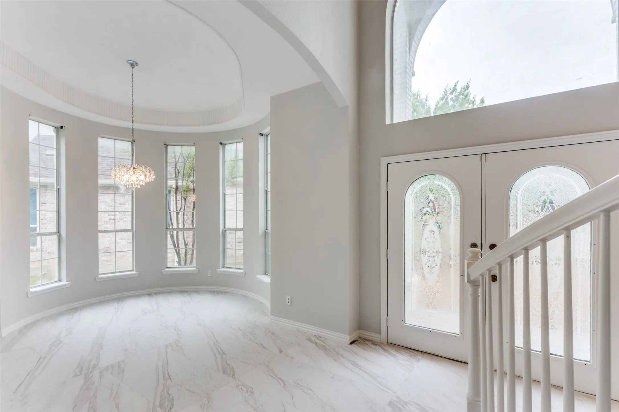Grand entry featuring double doors with decorative glass panels, a high arched window, and a white balustrade staircase