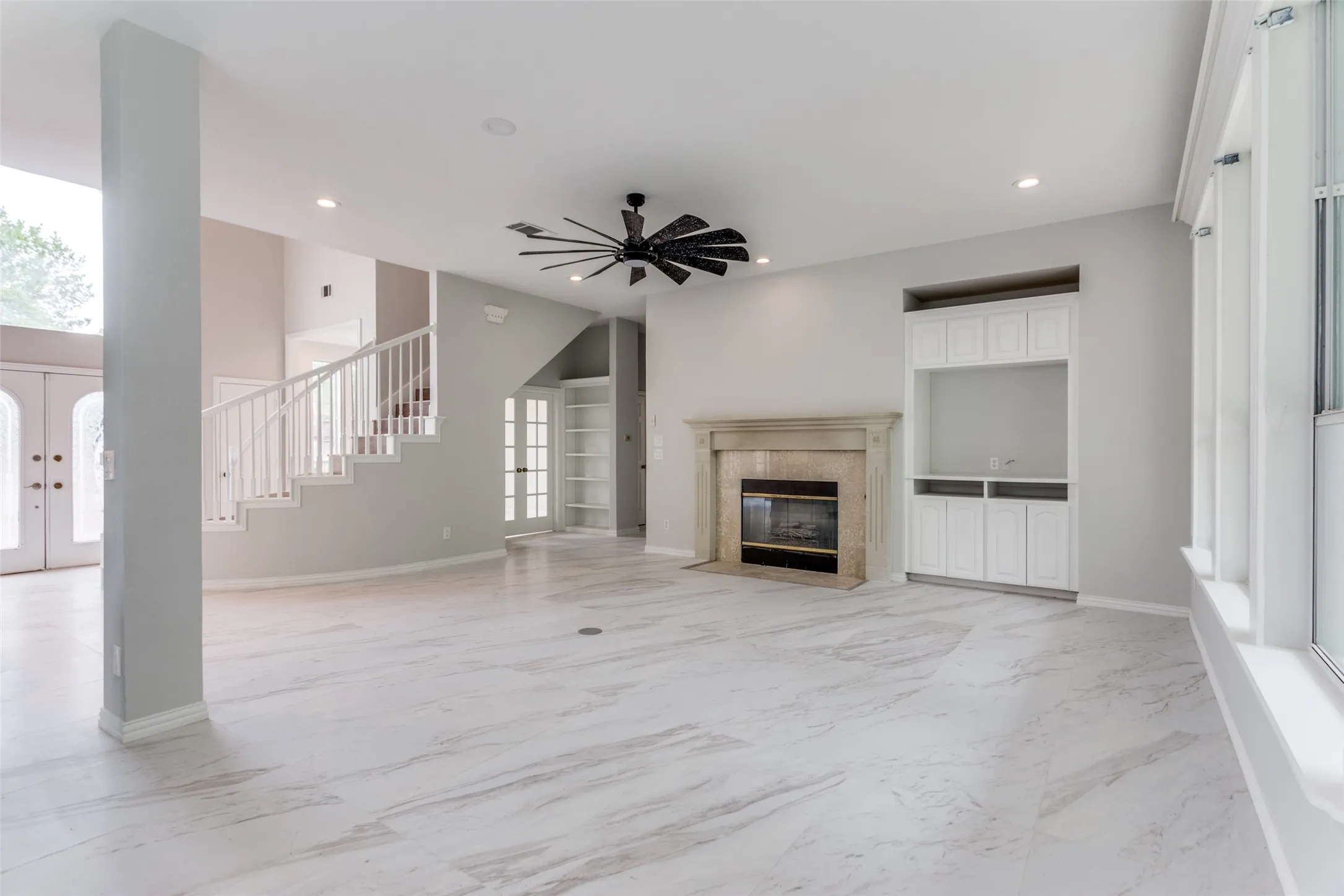 Spacious living area featuring light-toned tile flooring, a built-in media cabinet, a stone fireplace, and a contemporary ceiling fan