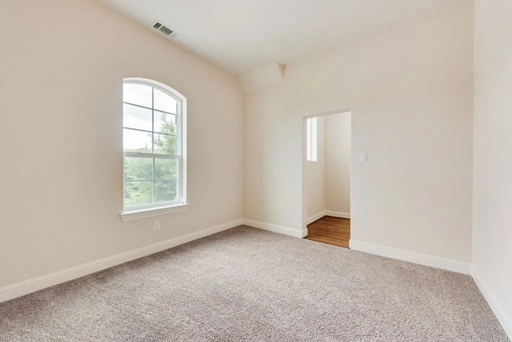 Carpeted room featuring an arched window, white trim, and a recessed doorway leading to an area with wood-finish flooring and a small window