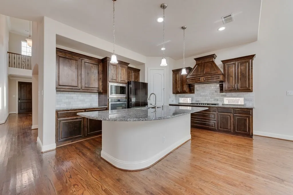 Gourmet kitchen featuring a large curved island with a granite countertop, dark wood cabinetry, stainless steel appliances, a tiled backsplash, and recessed lighting