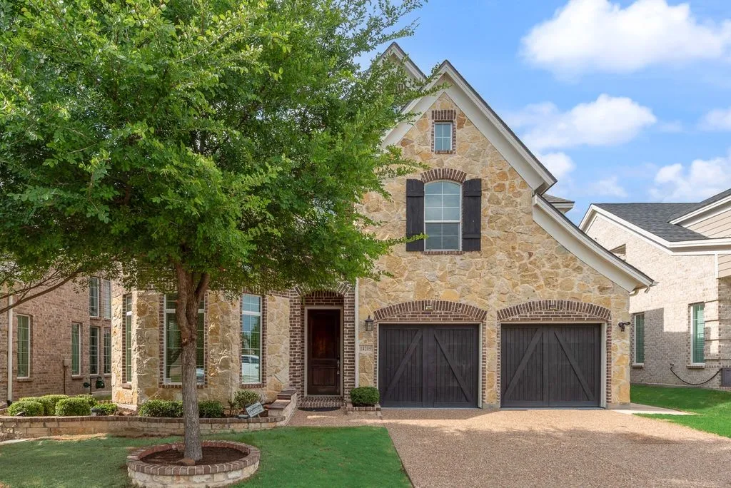 Stone and brick facade residence featuring a two-car garage with dark wood doors, arched brick accents, and a prominent front entry