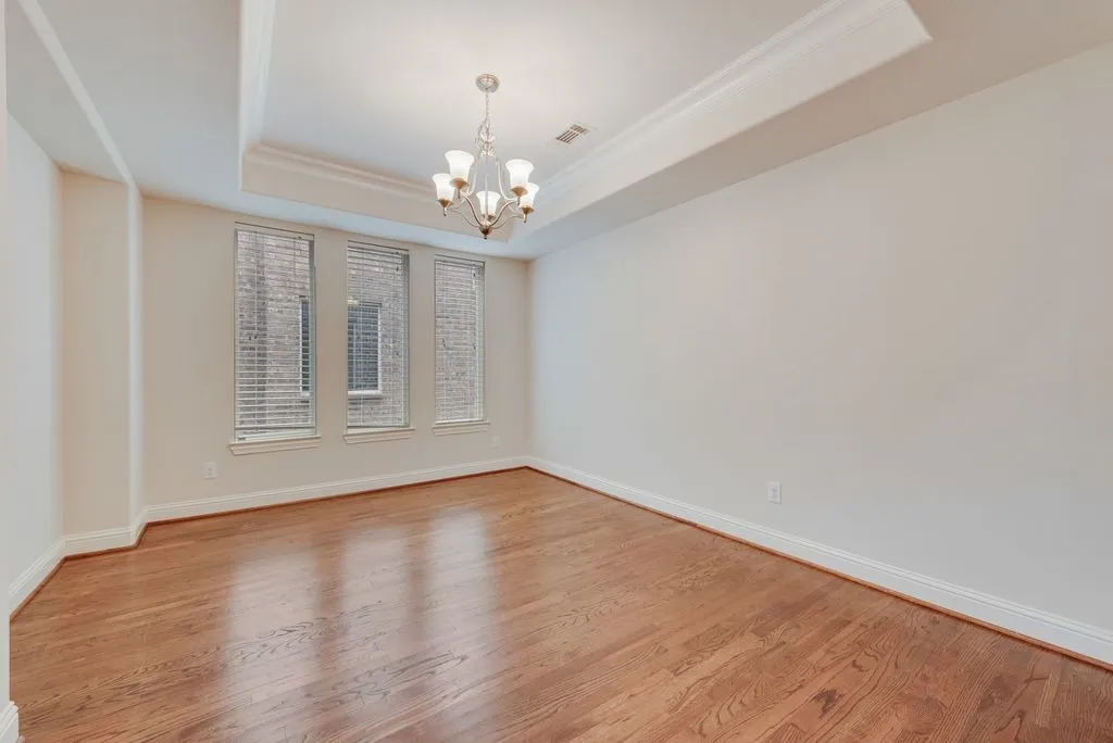 Room with wood-finish flooring, white baseboards, and a tray ceiling with crown molding