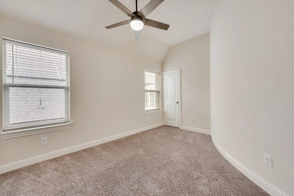 Carpeted room featuring a vaulted ceiling and a ceiling fan with integrated lighting