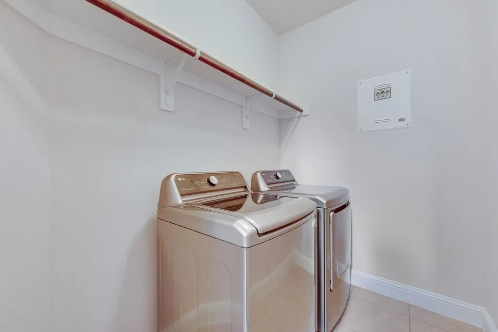Laundry area featuring light-toned tile flooring, white baseboards, and a wall-mounted shelf with a hanging rod