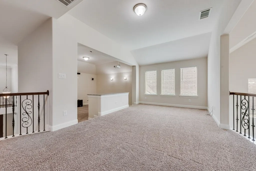 Upper-level versatile space featuring three windows with blinds, carpeted flooring, and a wrought iron banister with wood-finish railing
