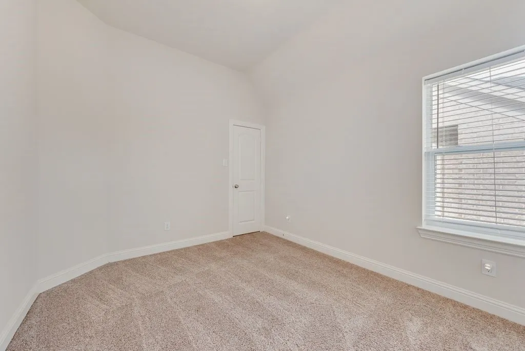 Carpeted room with a vaulted ceiling, white walls, and a single window with blinds