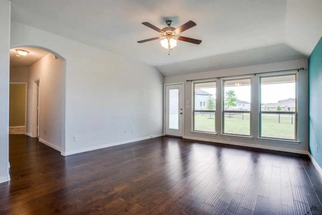 Dark wood-finish flooring, vaulted ceiling, built-in ceiling fan with light fixture, three large windows, and an arched entryway