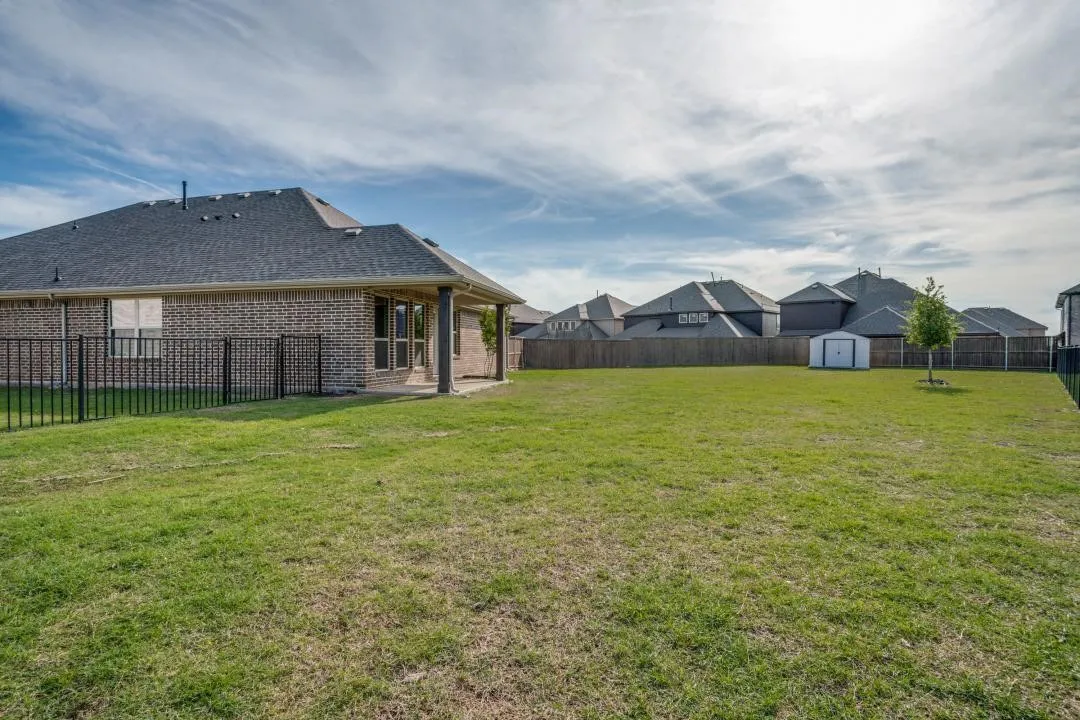Expansive grassy lawn with a privacy fence, covered patio, and a storage shed
