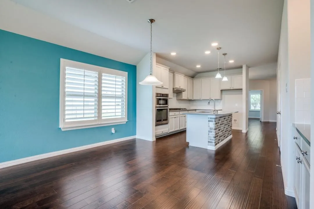 Kitchen and dining area featuring wood-finish flooring, vaulted ceiling, recessed lighting, and a kitchen island with stone tile detailing