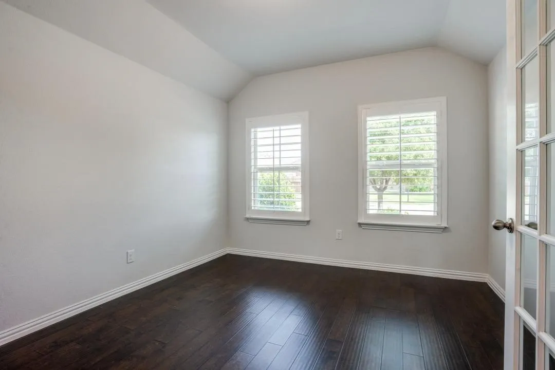 Vaulted ceiling, two windows with plantation shutters, dark wood-finish flooring, and a French door entry