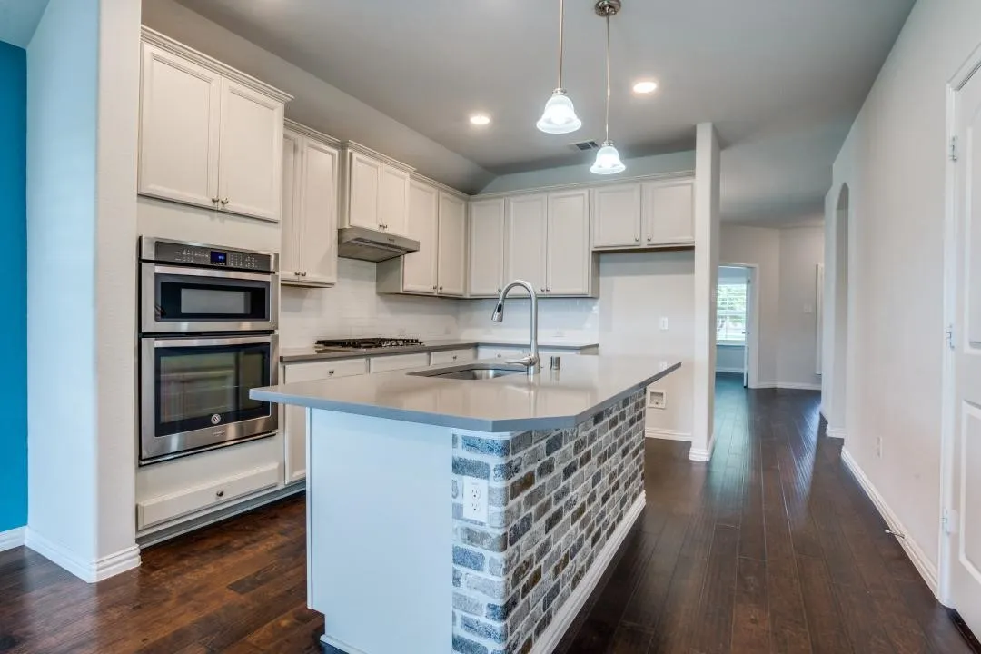 Kitchen featuring light cabinetry, stainless steel appliances, a center island with brick detailing, wood-finish flooring, and pendant lighting
