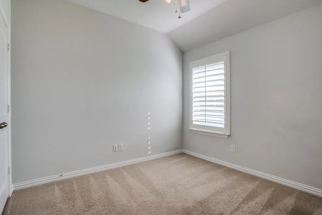 Window with plantation shutters, ceiling fan with light fixture, light-colored carpet, and painted walls