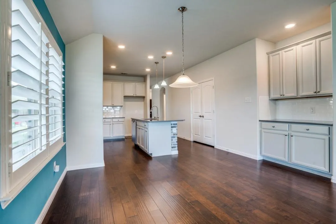 Hardwood flooring throughout, white cabinetry with dark countertops, recessed lighting, white subway tile backsplash, and plantation shutters