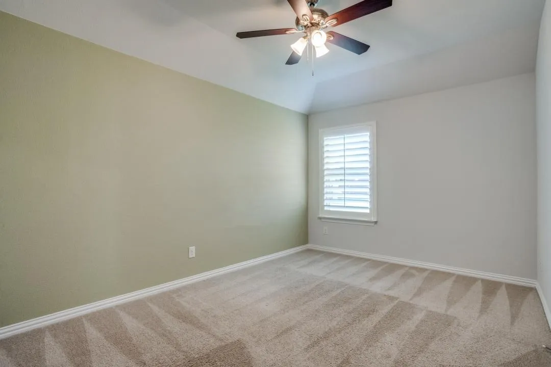 Carpeted room with vaulted ceiling and a ceiling fan
