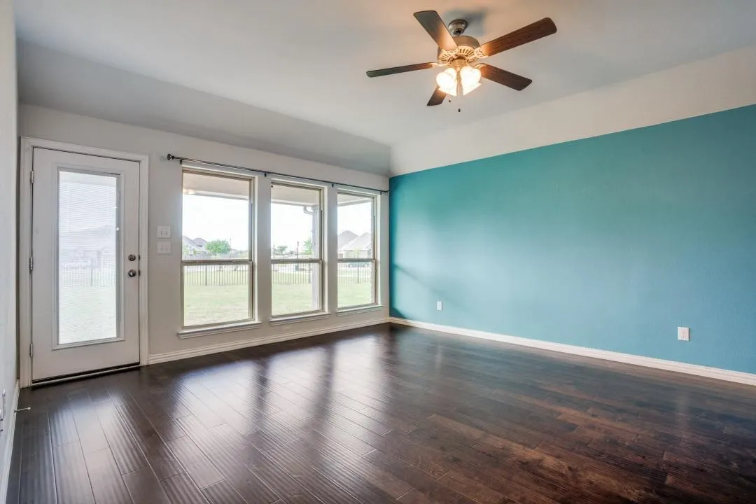 Dark wood-finish flooring, a ceiling fan with integrated lighting, and multiple windows with transoms