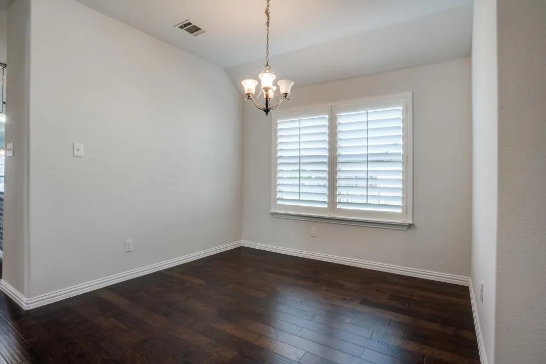 Dark wood-finish flooring, white plantation shutters, white crown molding, and a three-light chandelier