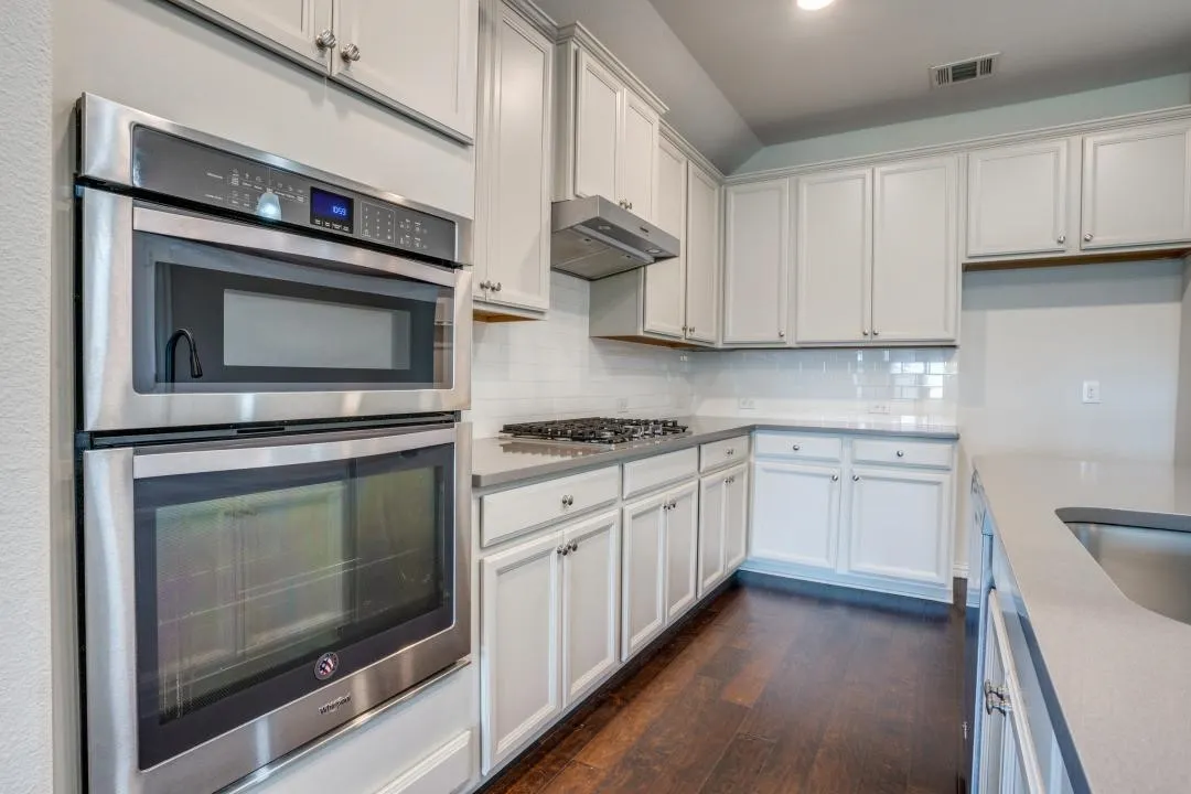 Kitchen featuring light-toned cabinetry, stainless steel built-in appliances, a gas range with a range hood, light-toned countertops, and dark wood-finish flooring
