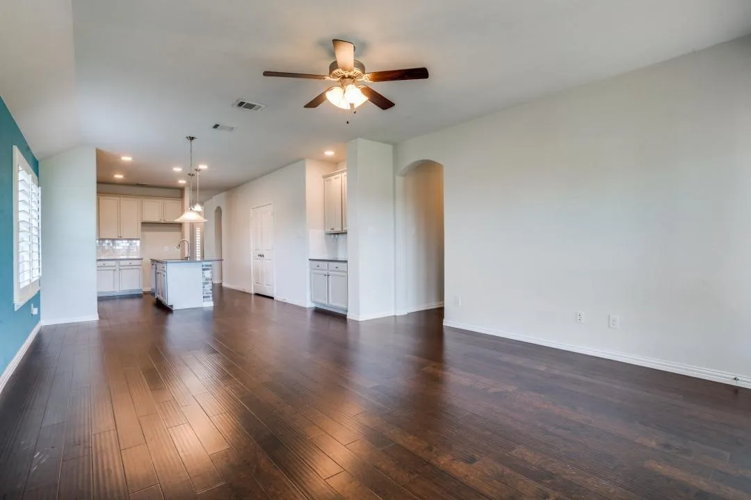 Dark wood-finish flooring throughout, a ceiling fan with integrated lighting, and a kitchen island with pendant lighting