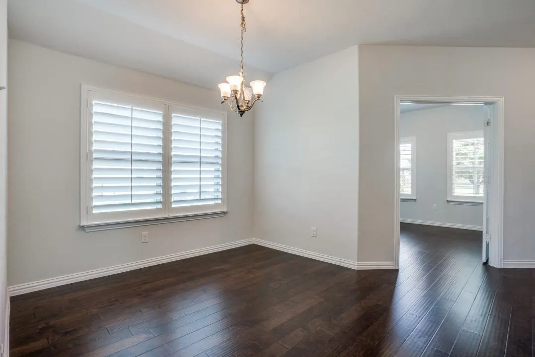 Hardwood-style flooring throughout, white plantation shutters, and a chandelier with glass shades