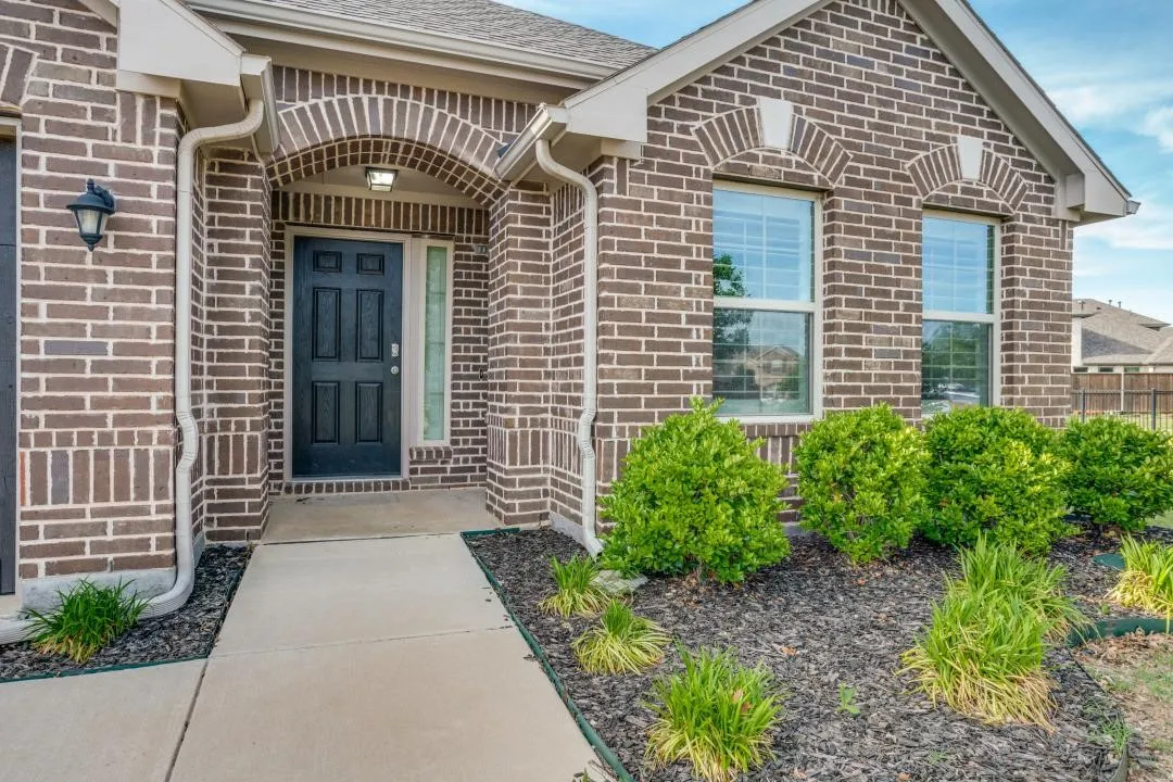 Brick exterior with architectural accent arches, an arched entry, a dark paneled door, and front landscaping