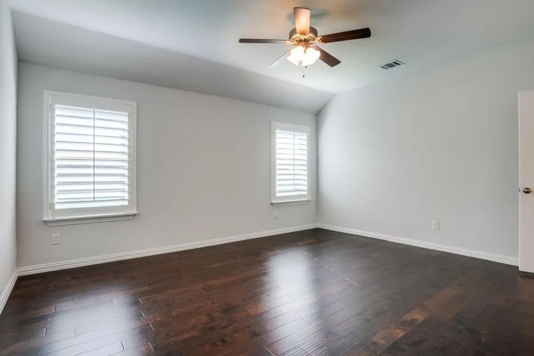 Vaulted ceiling with a ceiling fan, two windows with plantation shutters, and wood-finish flooring