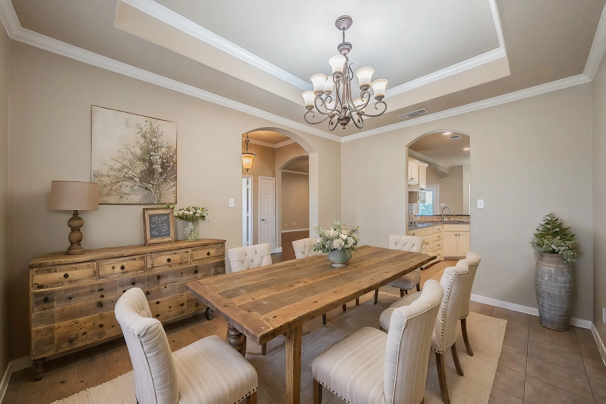 Tray ceiling with crown molding, chandelier lighting, arched doorways, tile flooring, and wood-finish flooring
