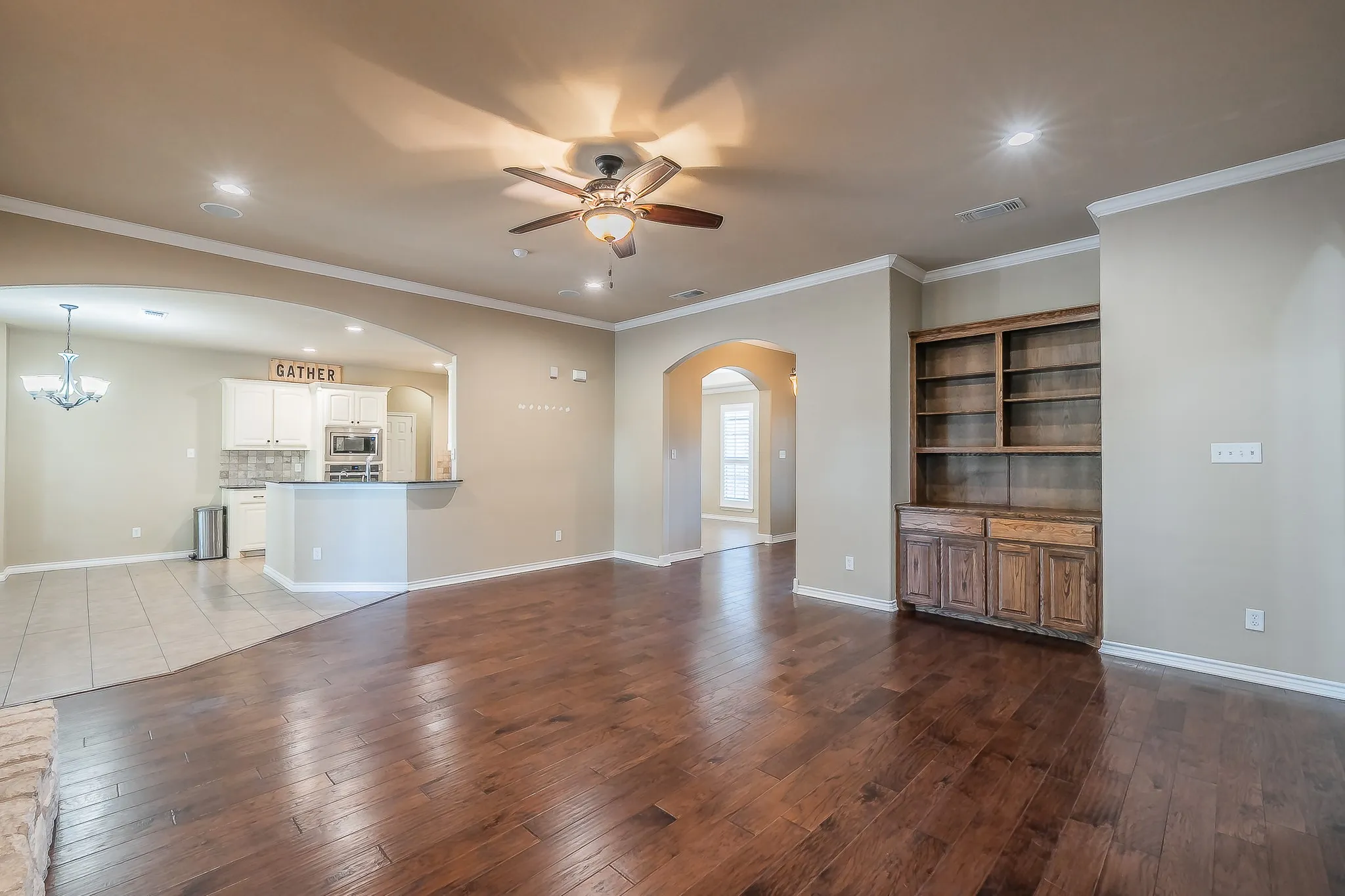 Expansive living area featuring rich wood-finish flooring, a ceiling fan with integrated lighting, and crown molding