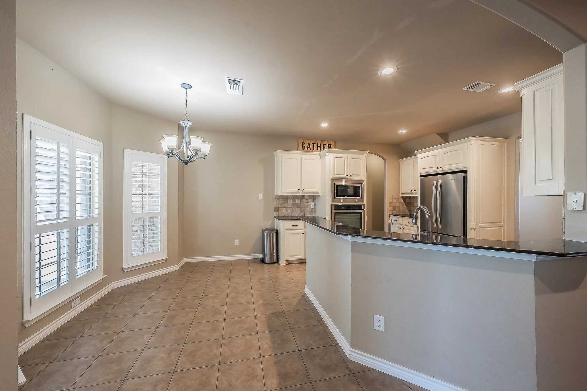 White cabinetry kitchen with dark countertops, stainless steel appliances, and a tile backsplash