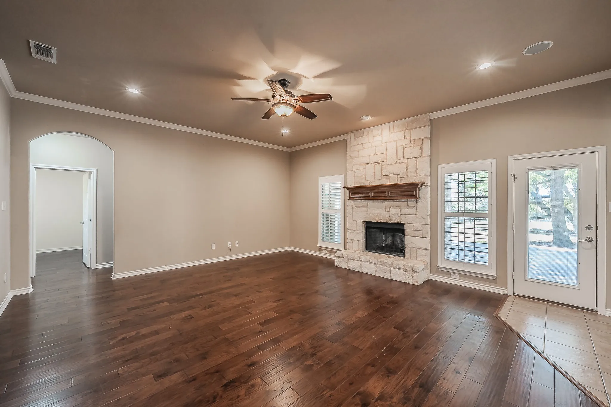 Wood-finish flooring, stone-clad fireplace with wood mantle, ceiling fan with integrated lighting, recessed ceiling lights, and an arched doorway