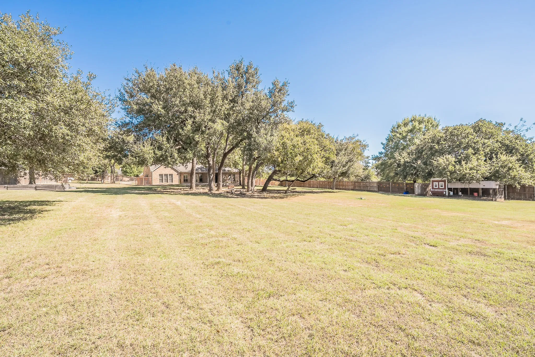 Expansive grassy area featuring mature trees and a private wood fence