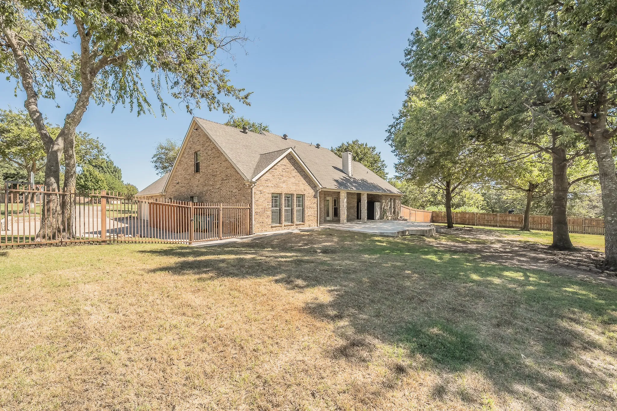 Brick exterior with multiple windows, leading to a covered patio and an expansive stone patio