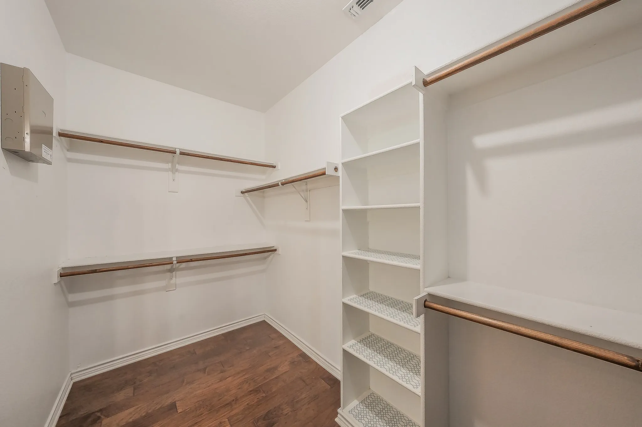 Walk-in closet featuring wood-finish flooring, built-in shelving, and multiple hanging rods
