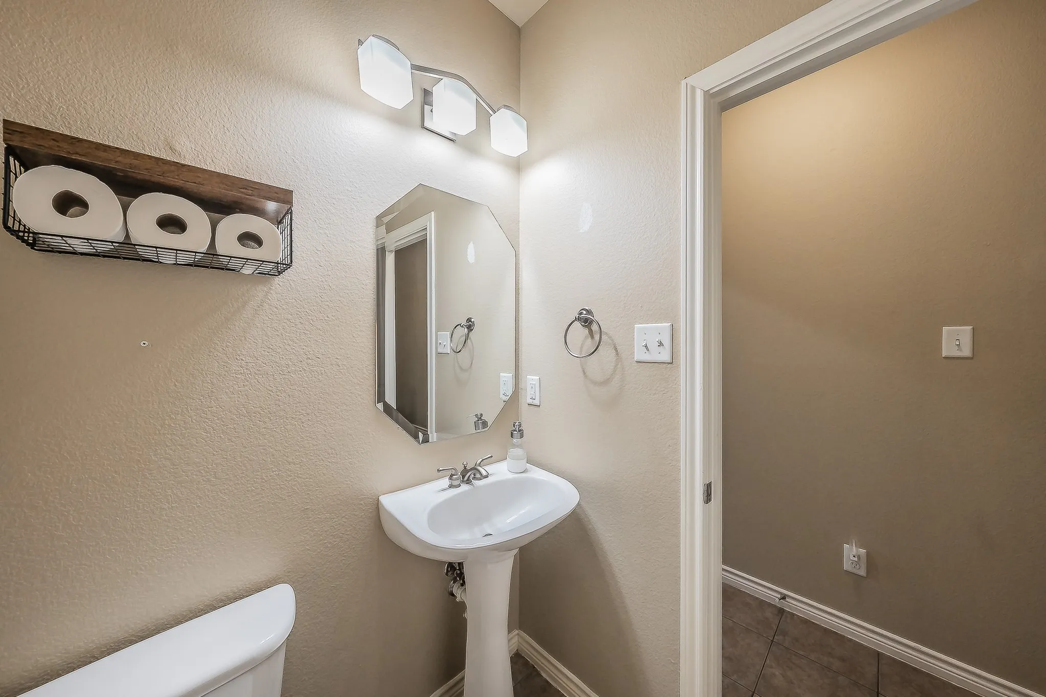 Pedestal sink with chrome-finish faucet, octagonal mirror, three-light vanity fixture, and tiled flooring