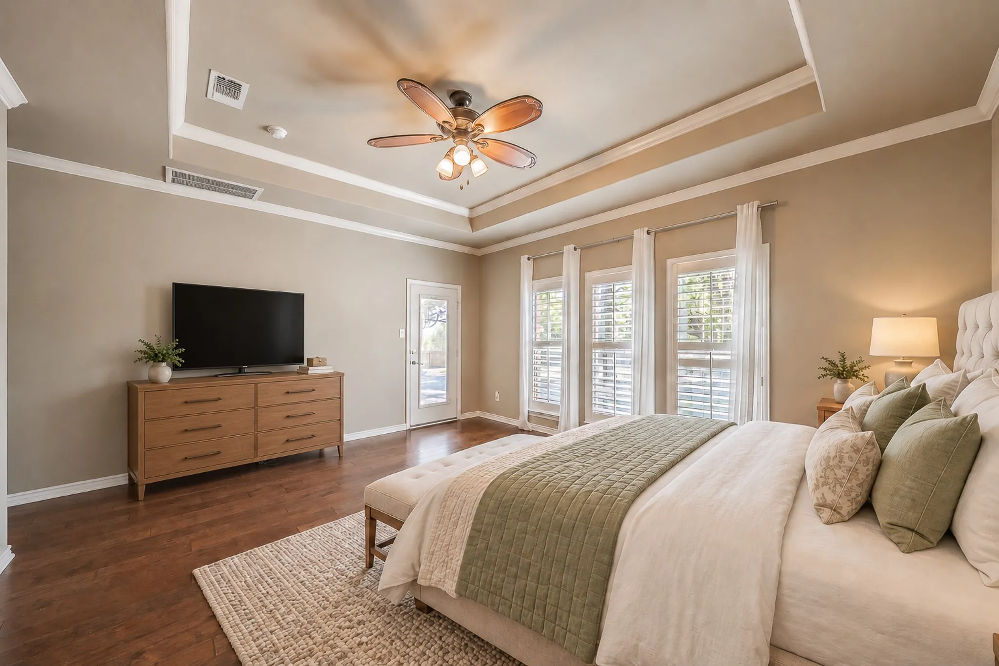 Tray ceiling with crown molding, wood-finish flooring, ceiling fan, multiple windows with plantation shutters, and a glass-paneled exterior door