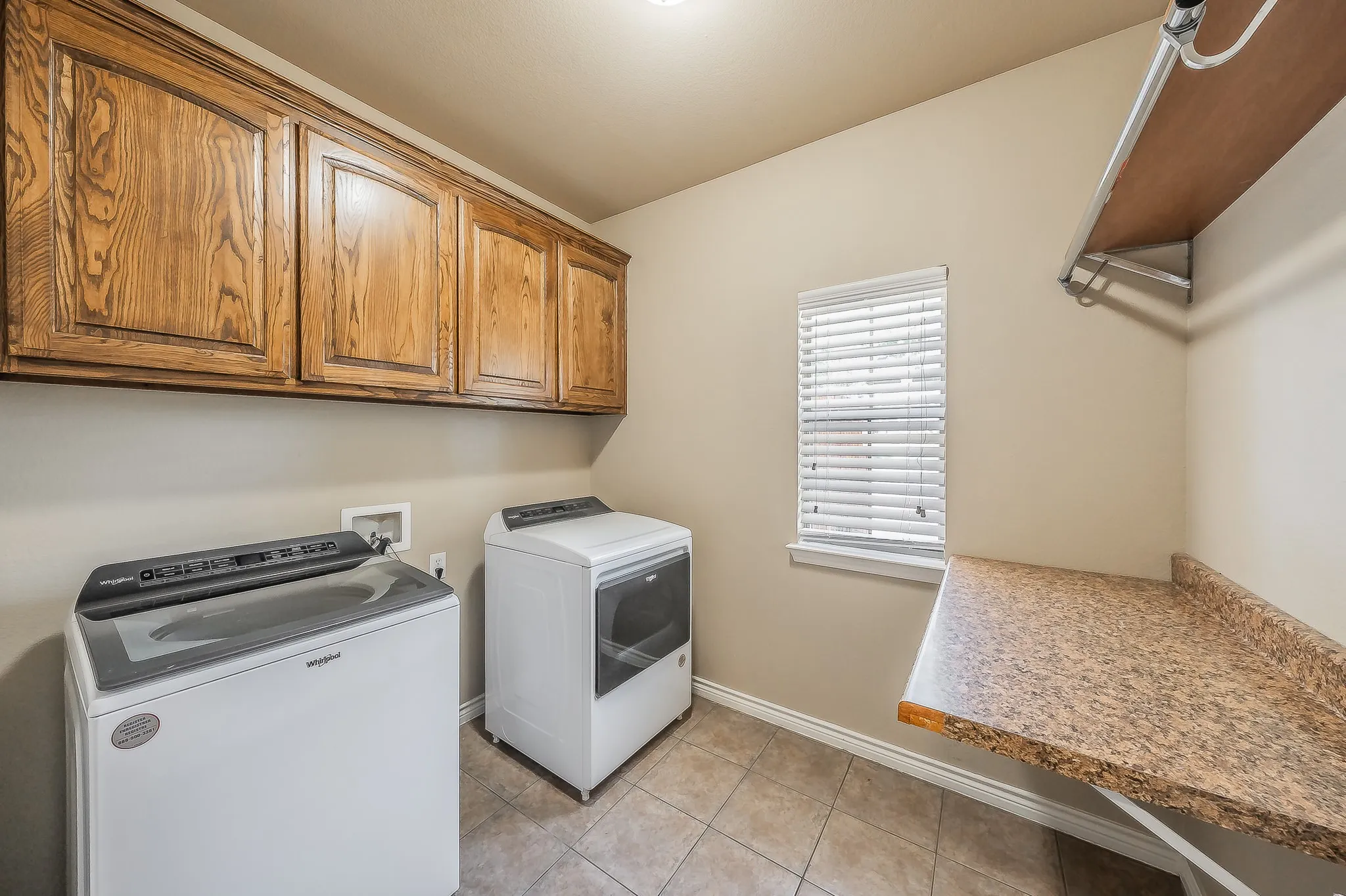 Built-in wood cabinetry, tiled flooring, window with blinds, granite-look countertop, and overhead shelving