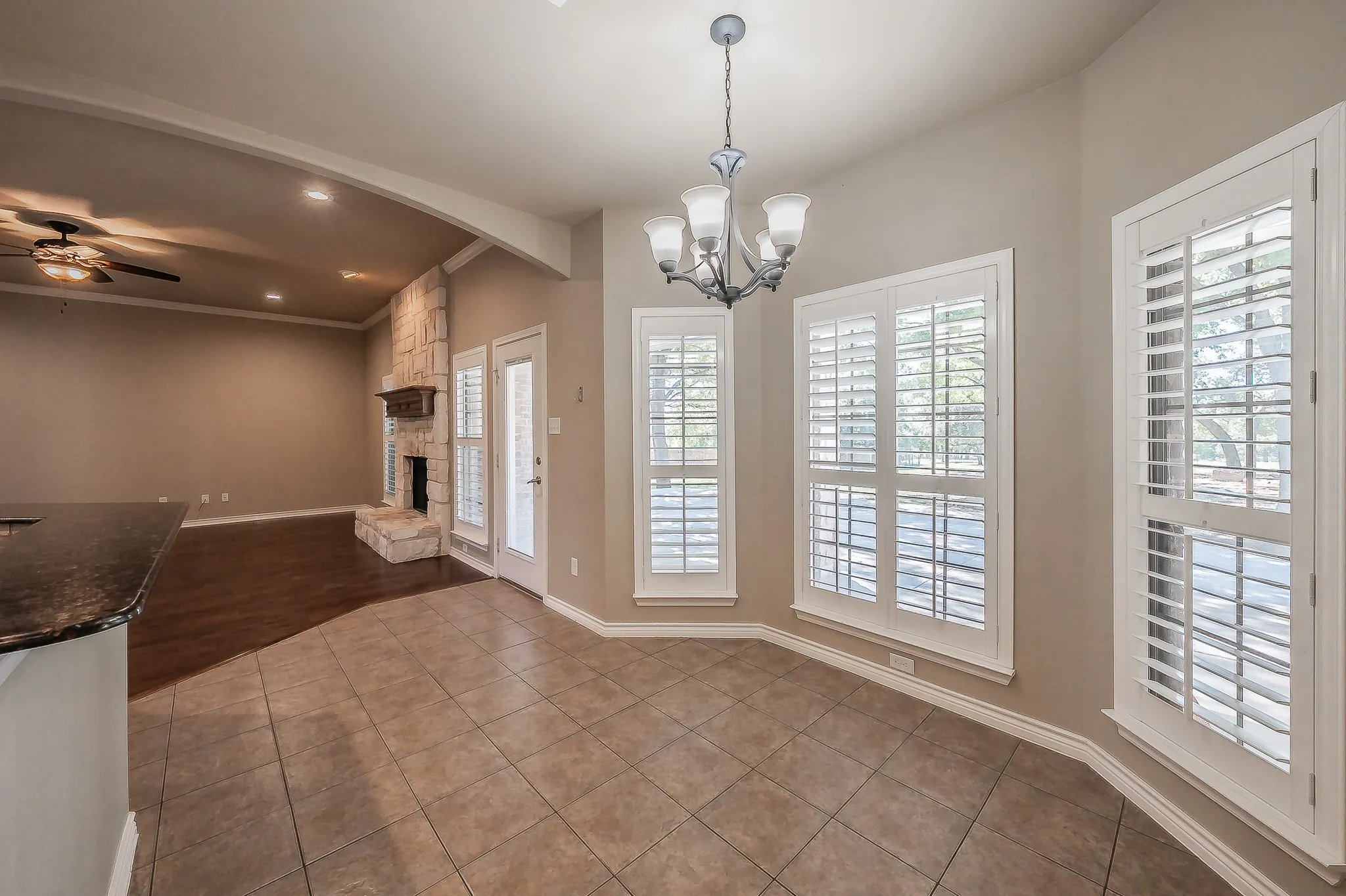 Tile flooring extending into a bay window, chandelier lighting, and plantation shutters