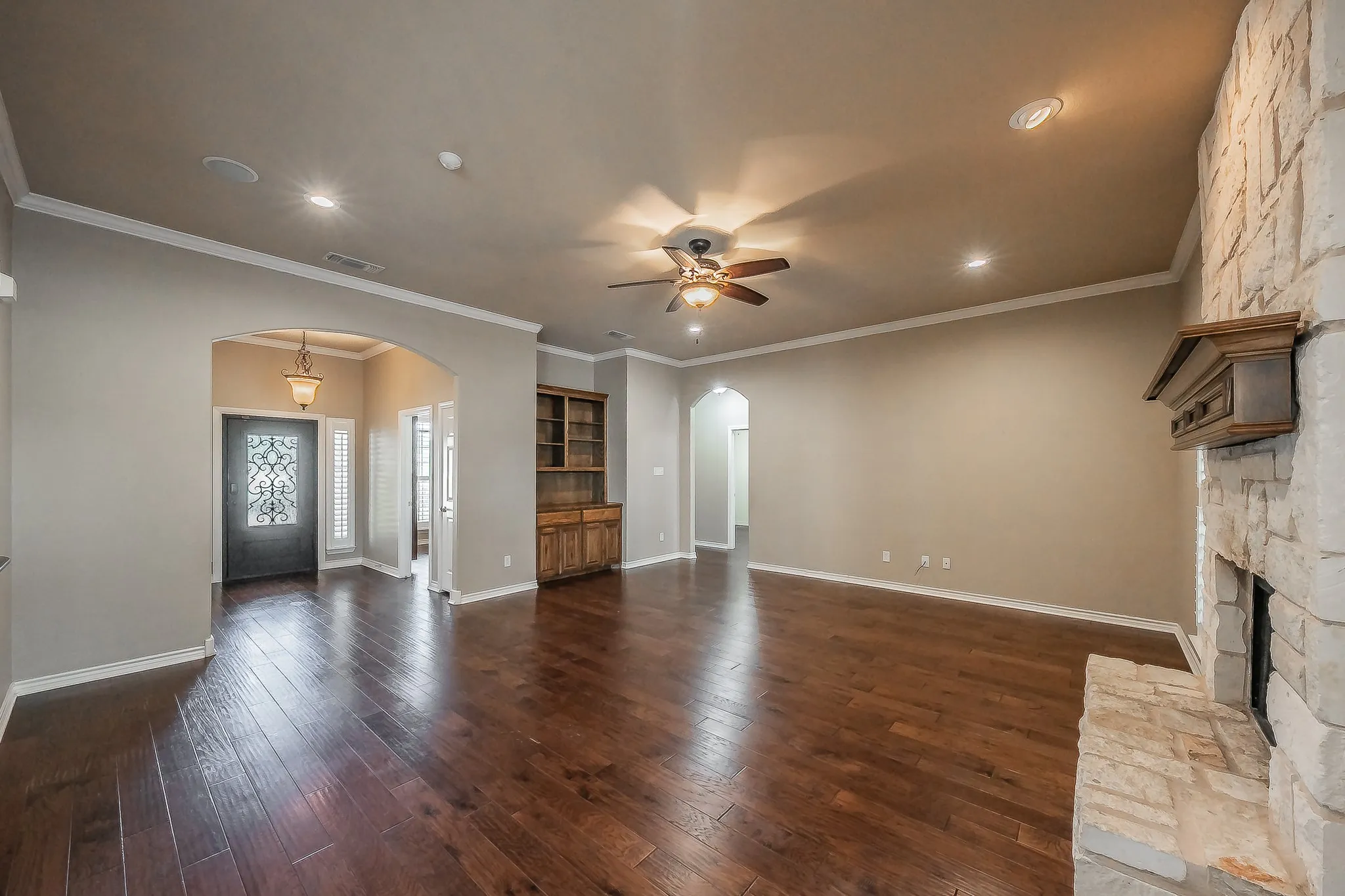 Hardwood-style flooring, stone-clad fireplace with wood mantel, recessed lighting, ceiling fan, and arched doorways